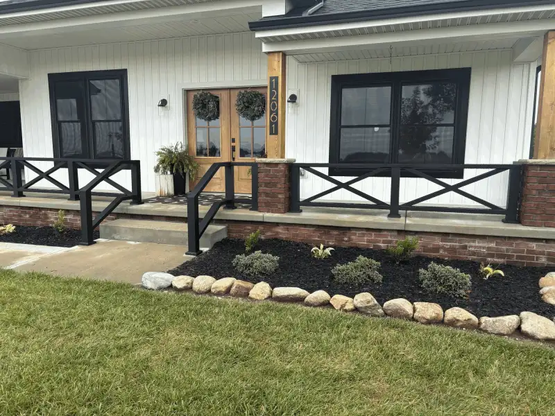 Black aluminum X-brace porch railing beside front entry with brick knee wall, Northern Indiana installation